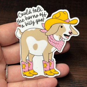 May include: A sticker depicting a cartoon goat in a yellow cowboy hat, pink polka-dot bandana, and pink cowboy boots with yellow details. The sticker includes the text "Could talk the horns off a billy goat."