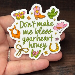 May include: A white sticker with a country theme, featuring a cowboy boot, cactus, horseshoe, and butterfly illustrations. The sticker has the text "Don't make me bless your heart honey" in green script.