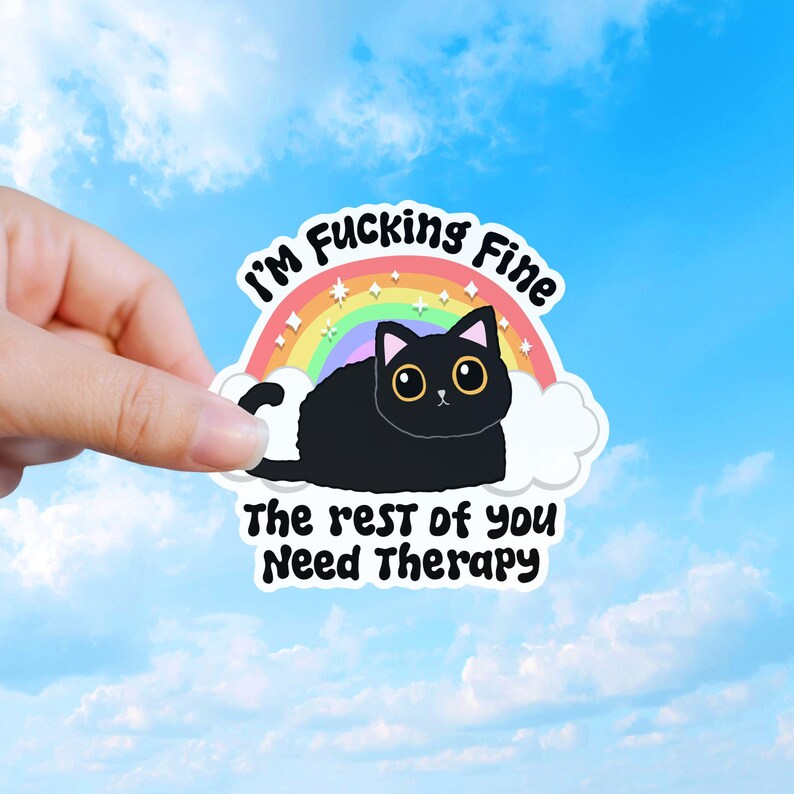 May include: A die-cut sticker featuring a black cat with large eyes sitting in front of a colorful rainbow and white clouds. The text reads I'M FUCKING FINE above the rainbow and THE REST OF YOU NEED THERAPY below the cat in black lettering.