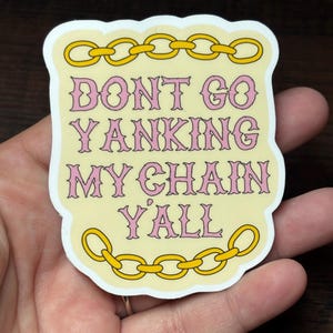 May include: A sticker with a light yellow background and a white border. The text "DONT GO YANKING MY CHAIN Y'ALL" is in pink, outlined in a darker pink. Gold chain links are at the top and bottom of the sticker.