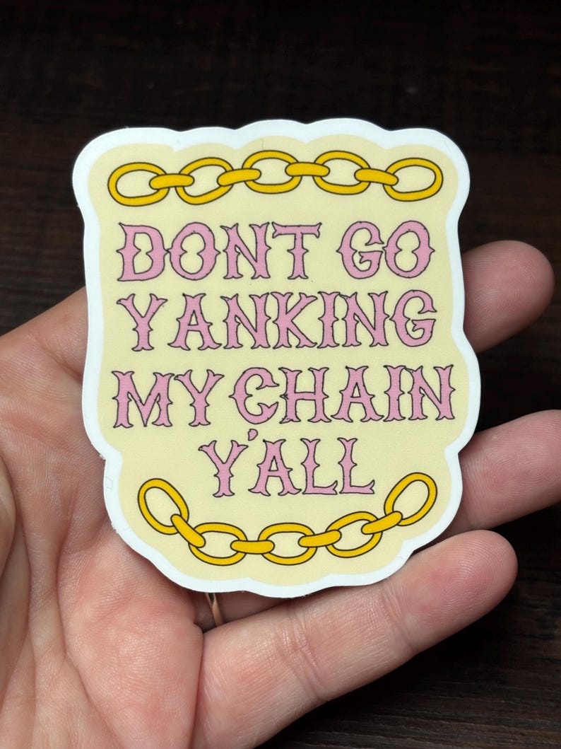 May include: A sticker with a light yellow background and a white border. The text "DONT GO YANKING MY CHAIN Y'ALL" is in pink, outlined in a darker pink. Gold chain links are at the top and bottom of the sticker.