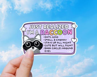 May include: A rectangular sticker with a light purple background featuring a cartoon raccoon head and the text: JUST REALIZED I'M A RACCOON. Bullet points list: EATS JUNK, SMALL & CHONKY, STAYS UP ALL NIGHT, CUTE BUT WILL FIGHT, DARK CIRCLES AROUND EYES.