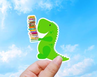 Puede incluir: Una pegatina troquelada que muestra un dinosaurio de dibujos animados de color verde brillante sosteniendo una pila alta y vertical de libros multicolores. El dinosaurio tiene un cuerpo redondeado, una cola pequeña y manchas verde oscuro en la espalda.