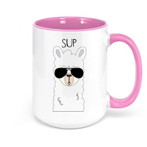 May include: White ceramic mug with a pink interior and handle. The mug features a cartoon llama wearing sunglasses, with the word "SUP" above the llama's head. The mug is a fun and quirky item.