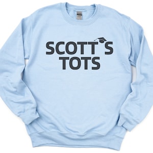May include: Light blue sweatshirt with the text "SCOTT'S TOTS" in black lettering and a graduation cap above the "S".