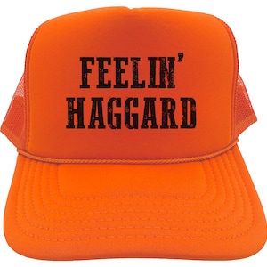 May include: Orange trucker hat with black text that reads "FEELIN' HAGGARD".