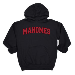 May include: Black hooded sweatshirt with the name "MAHOMES" in red, arched lettering across the chest. The sweatshirt has a front pocket and a drawstring hood. The sleeves are cuffed.