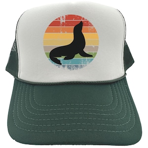 May include: A white and green trucker hat with a retro-style graphic of a seal silhouette in front of a rainbow sunset.