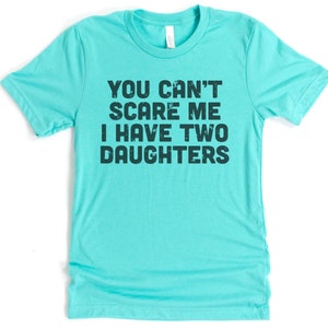 May include: A turquoise blue t-shirt with the text "You can't scare me I have two daughters" printed in black.