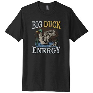 May include: A black t-shirt with a vintage-style illustration of a duck in a pond. The text "BIG DUCK ENERGY" is printed in yellow and white on the shirt.
