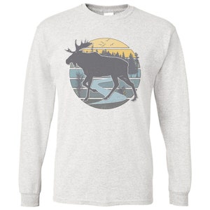 May include: A gray long-sleeve t-shirt with a vintage-style graphic of a moose walking through a forest with a river and a sunset in the background.