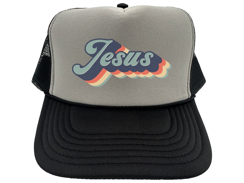 Puede incluir: Una gorra de camionero gris y negra con un dise&ntilde;o retro de arco&iacute;ris que dice "Jes&uacute;s" en una fuente azul, blanca y naranja.