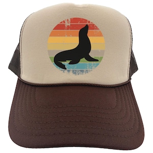 May include: A brown and beige trucker hat with a vintage-style graphic of a seal in a rainbow sunset. The hat has a mesh back.