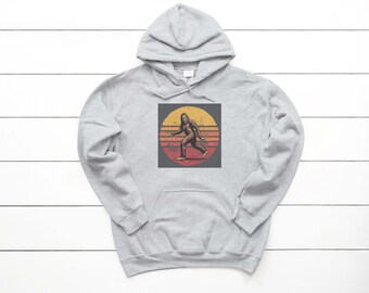 Peut inclure: Un sweat à capuche gris clair avec un motif de Bigfoot. Le motif montre un Bigfoot brun marchant devant un coucher de soleil jaune et rouge. Le sweat à capuche a une poche avant et une capuche à cordon.