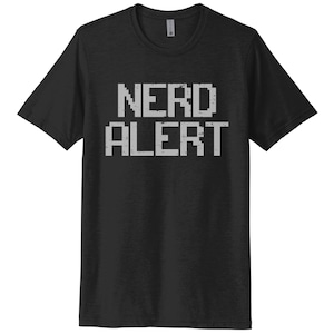Op de afbeelding: Zwart T-shirt met ronde hals en de tekst "NERD ALERT" in een gepixelde, verweerde witte letter. Dit T-shirt met korte mouwen is een casual stijl, geschikt voor dagelijks gebruik.