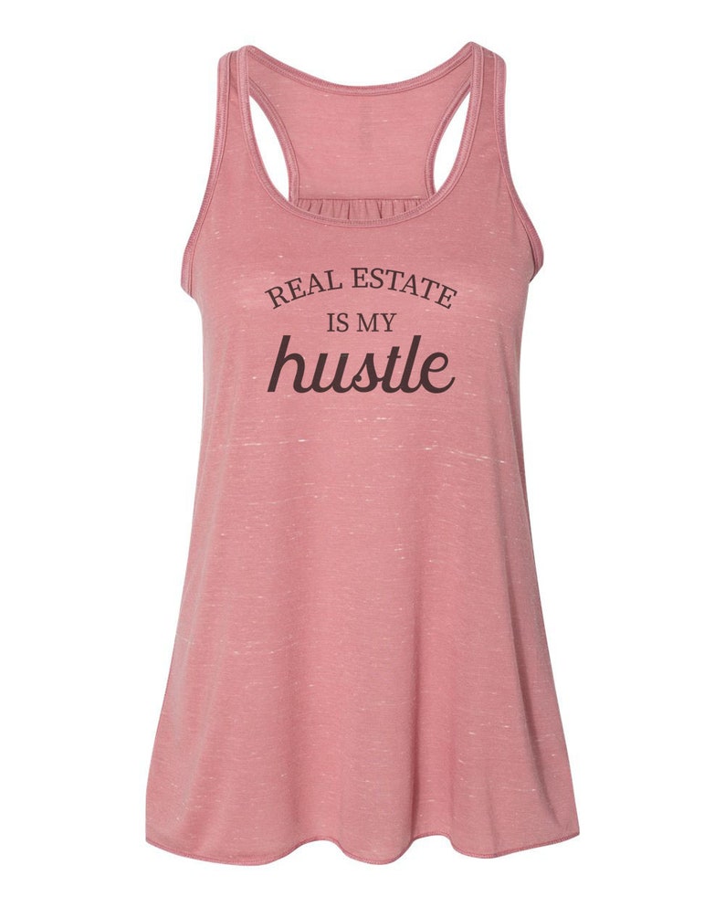 May include: A pink racerback tank top with the text "REAL ESTATE IS MY hustle" printed on the front.