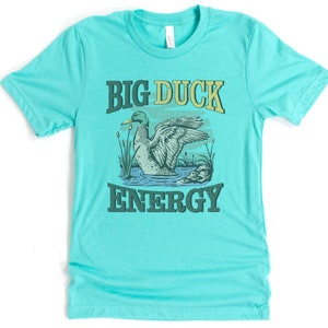 May include: A turquoise blue t-shirt with a green duck illustration and the text "BIG DUCK ENERGY" in a vintage style font.