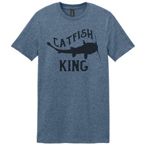 May include: A blue heather t-shirt with a black silhouette of a catfish and the text "Catfish King".