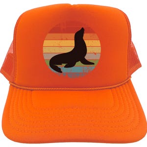 May include: Orange trucker hat with a vintage-style graphic of a seal in front of a sunset. The seal is black and the sunset is a rainbow of colors.