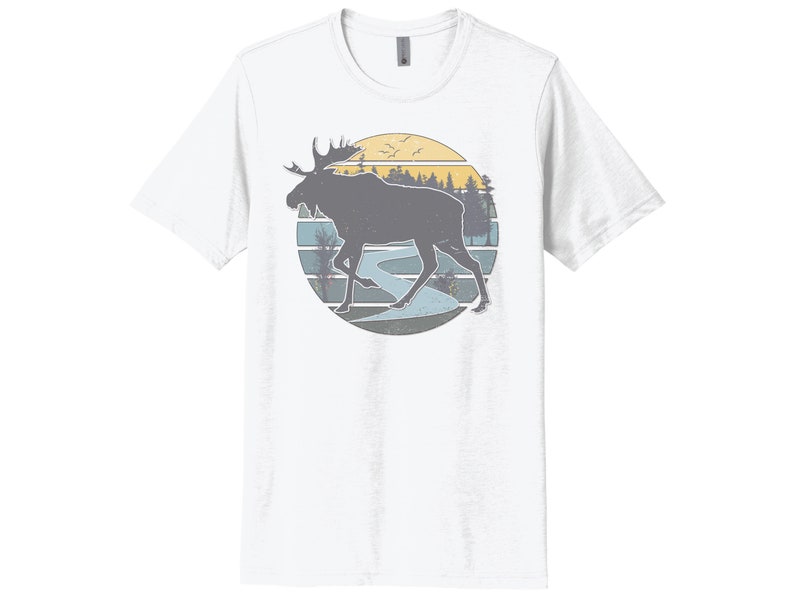 May include: A white t-shirt with a vintage-style graphic of a moose walking through a forest with a river in the background. The graphic is in shades of blue, yellow, and brown.