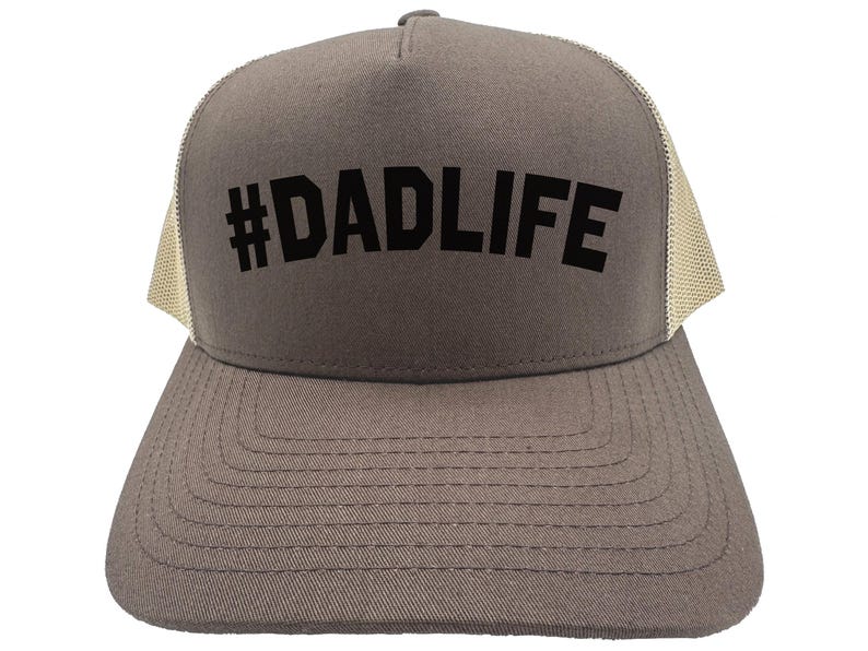 May include: A gray trucker hat with a mesh back and a curved brim. The front of the hat features the text "#DADLIFE" in bold, black letters. The hat is designed for casual wear.