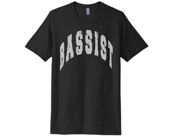 Puede incluir: Camiseta negra con un gráfico blanco desgastado que dice "Bassist" en una fuente arqueada.