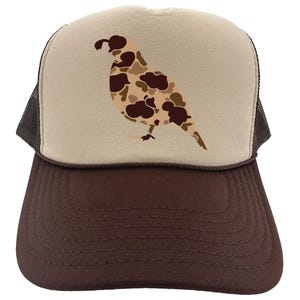 May include: A brown and beige trucker hat with a camouflage quail design on the front. The hat has a brown mesh back.