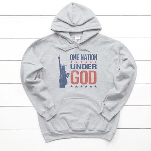 May include: A gray hooded sweatshirt with a distressed graphic print of the Statue of Liberty and the text "ONE NATION UNDER GOD" in red and blue.