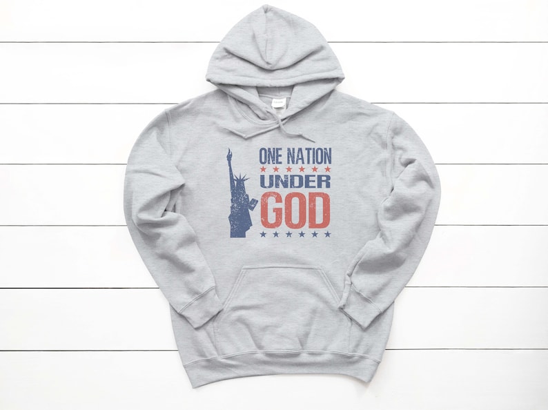 May include: A gray hooded sweatshirt with a distressed graphic print of the Statue of Liberty and the text "ONE NATION UNDER GOD" in red and blue.