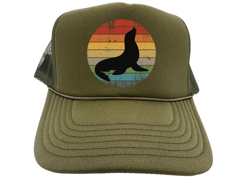 May include: A green trucker hat with a vintage-style sunset graphic featuring a silhouette of a seal. The hat has a mesh back and a brown adjustable strap.
