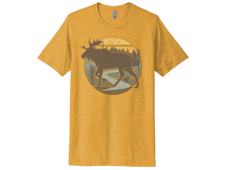 May include: A yellow t-shirt with a vintage-style illustration of a moose walking through a forest with a river in the background. The illustration is surrounded by a circle with a sunset behind the moose.