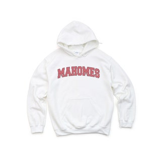 May include: White hooded sweatshirt with the word "MAHOMES" in red block letters across the chest. The sweatshirt has a front pocket and a drawstring hood. The fabric appears to be a soft, comfortable material.