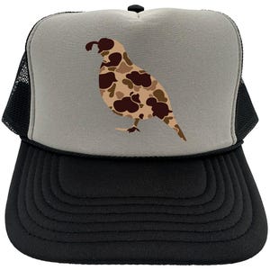 May include: A black and gray trucker hat with a camouflage quail design on the front. The hat has a mesh back.