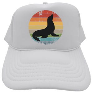May include: White trucker hat with a retro-style graphic of a seal in front of a rainbow sunset.