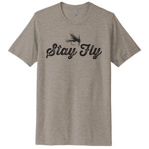 May include: A heather grey t-shirt with a black graphic of a fly fishing lure and the text "Stay Fly".