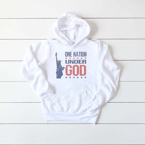 May include: White hoodie with a blue and red graphic of the Statue of Liberty and the text "ONE NATION UNDER GOD" with stars.