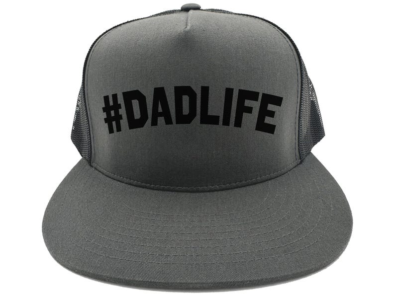 May include: A gray trucker hat with a black mesh back and a curved brim. The front of the hat features the text "#DADLIFE" in bold, black letters. The hat is a classic style, suitable for casual wear.