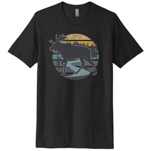 May include: Black t-shirt with a vintage-style graphic of a moose walking through a forest with a sunset in the background.