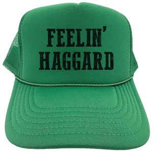 May include: Green trucker hat with a black embroidered design that says "Feelin' Haggard".