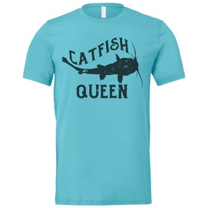 May include: A turquoise blue t-shirt featuring a black silhouette of a catfish and the text "Catfish Queen".