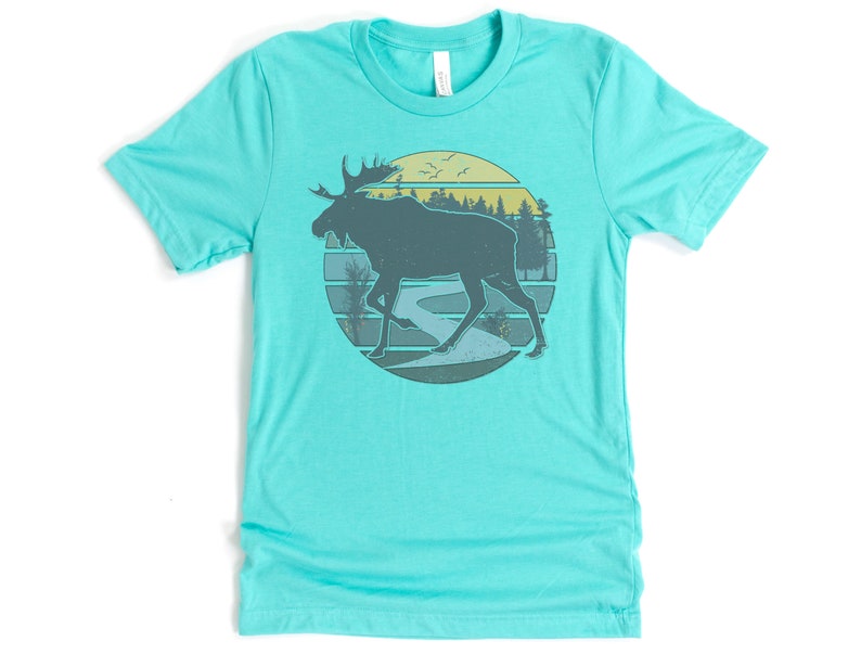 May include: A turquoise t-shirt with a retro-style graphic of a moose walking through a forest scene with a river and a sunset in the background.