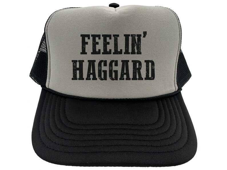 May include: A gray and black trucker hat with a black mesh back. The front of the hat has the text "FEELIN' HAGGARD" in black.