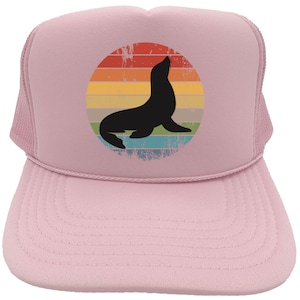 May include: Pink trucker hat with a retro-style graphic of a seal in front of a rainbow. The seal is black and the rainbow is in shades of yellow, orange, red, blue, and green.