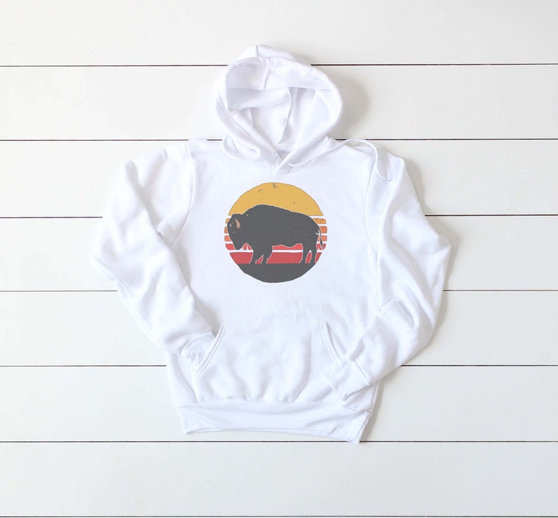 May include: White hooded sweatshirt with a retro-style graphic of a black silhouette of a bison in front of a yellow sun with red and orange stripes.