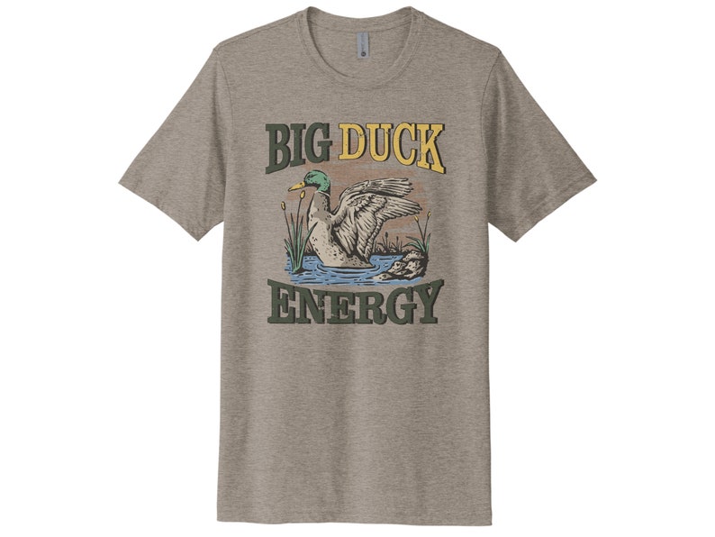 May include: A grey t-shirt with a vintage-style illustration of a duck swimming in a pond. The text "BIG DUCK ENERGY" is printed in yellow, green, and brown letters.