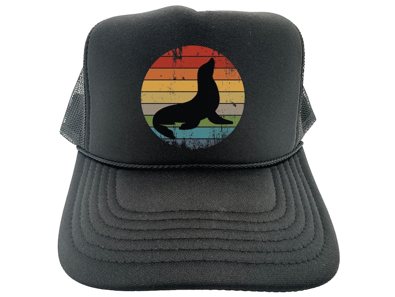 May include: Black trucker hat with a vintage-style graphic of a seal in front of a sunset. The graphic is in shades of orange, yellow, green, and blue.