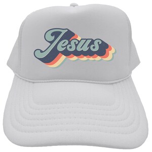 Puede incluir: Gorra de camionero blanca con un gr&aacute;fico retro de la palabra "Jes&uacute;s" en azul, naranja, amarillo y rojo.