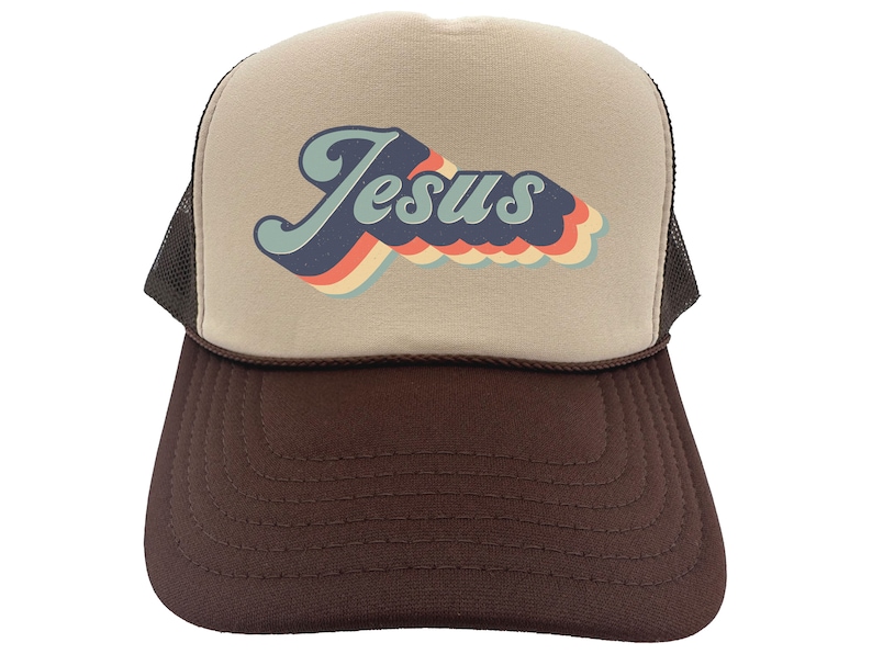 Puede incluir: Una gorra de camionero marr&oacute;n y beige con un gr&aacute;fico retro de "Jes&uacute;s" en azul, rojo, naranja y amarillo.