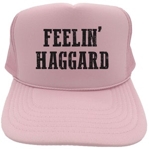 May include: A pink trucker hat with black text that reads "Feelin' Haggard".