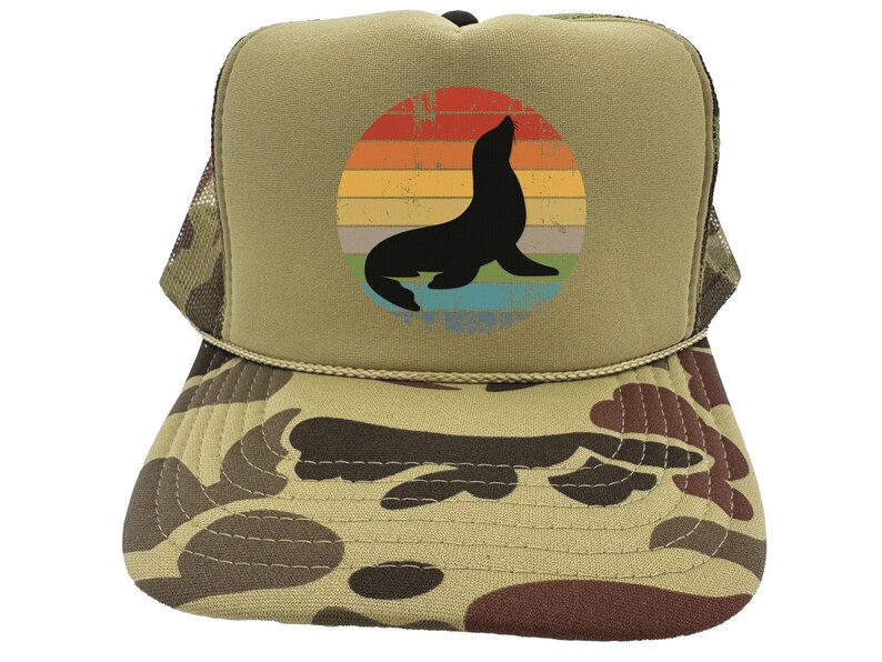 May include: A brown and tan camouflage trucker hat with a vintage-style graphic of a seal in front of a sunset. The graphic is in a circle with a blue, green, and yellow color scheme.